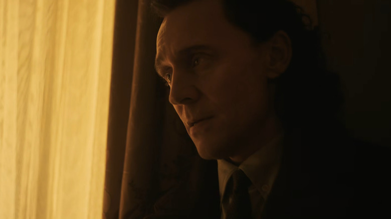 Tom Hiddleston as Loki wearing a shirt and tie and standing by a window bathed in yellow light in Avengers: Doomsday