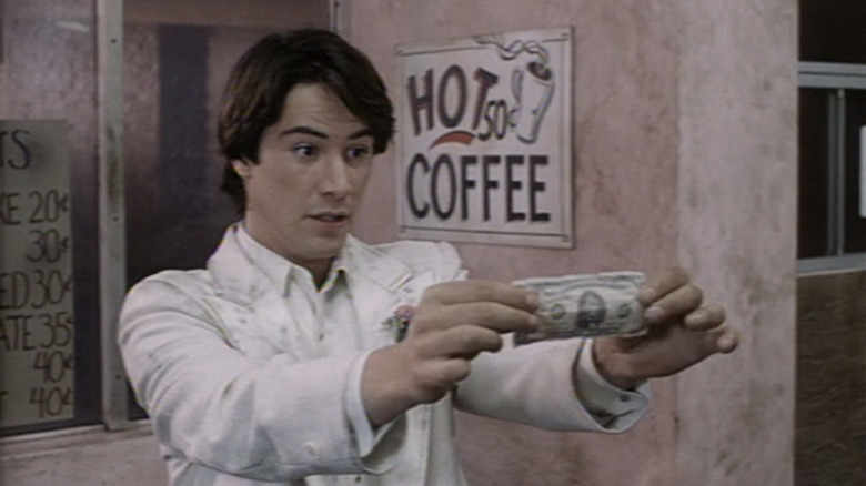 Keanu Reeves as Winston Connelly holds up a dollar bill in The Night Before