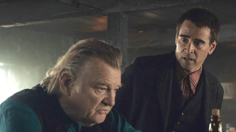 Colm sits blankly at a bar, while Padraic looks surprised at him while standing.
