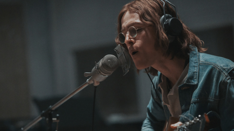 Harris Dickinson as John Lennon recording a song while playing guitar in The Beatles