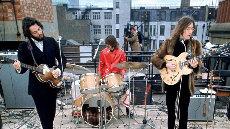 two men playing guitars on a rooftop and a drummer playing behind them