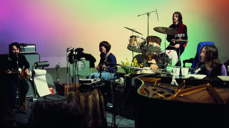 men sitting at instruments in front of a rainbow hued backdrop