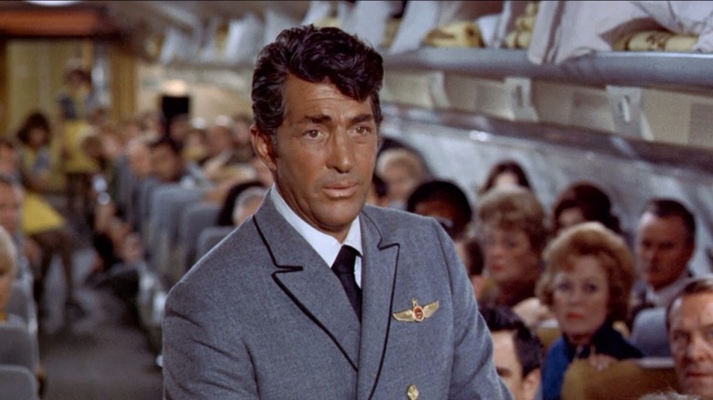Dean Martin as Vernon Demerest in Airport, standing in a place aisle with his uniform on and a full plane of passengers behind him.