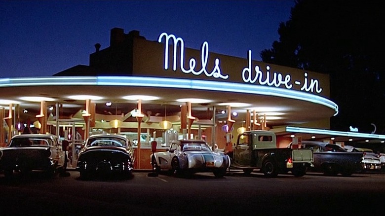 A wide shot of the neon-lit exterior of Mels Drive-In at dusk in American Graffiti.