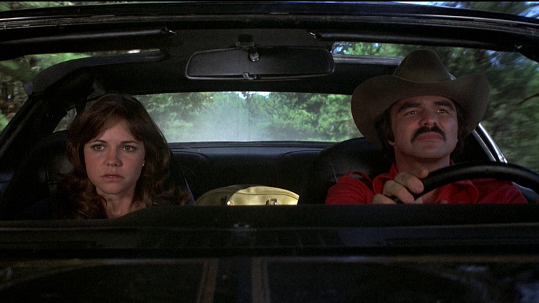Burt Reynolds as Bo "The Bandit" Darville and Sally Field as Carrie "Frog" in Smokey in the Bandit, sitting next to each to each other in a car as Bo drives.