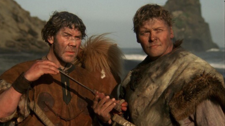 Þráinn Karlsson as Olaf the Childlover stands on a beach with Jakob Þór Einarsson as Gestur in When the Raven Flies