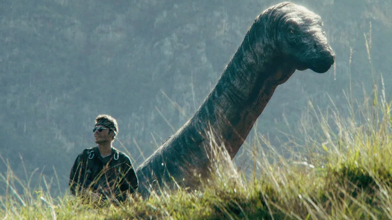 Nick Wechsler as Eli Taylor in Primitive War, standing among a cliffside with a long-necked dinosaur standing behind him.