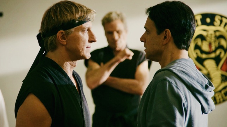 Johnny Lawrence and Daniel LaRusso confront while John Kreese looks on at Cobra Kai