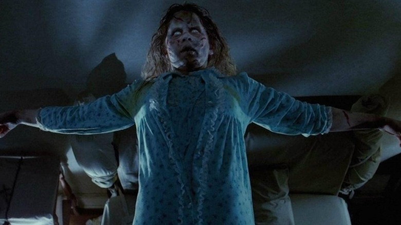 A possessed Regan MacNeil (Linda Blair) stands up with her arms outstretched in The Exorcist