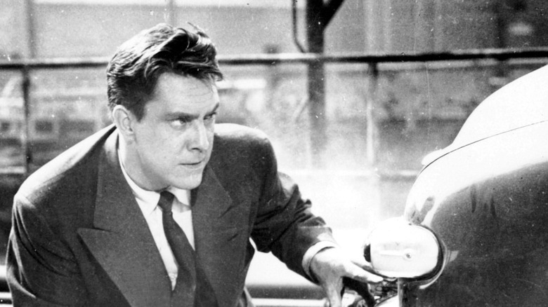 A man crouches behind a car