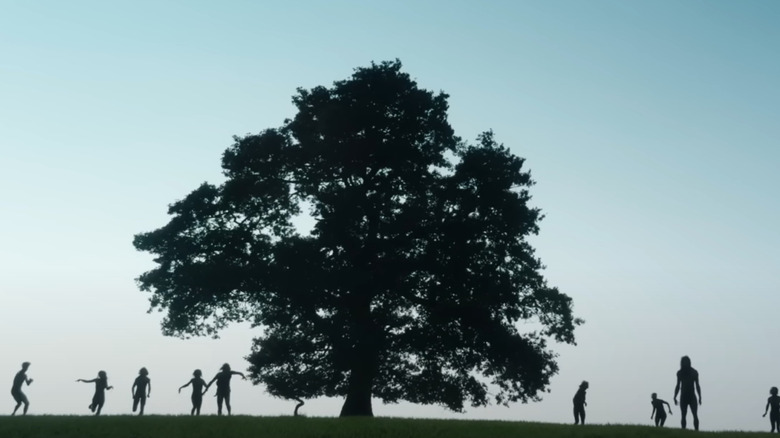 A silhouette shot of several infected standing by a tree on a hilltop in 28 Years Later