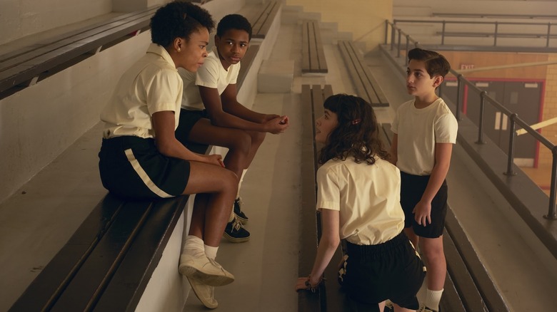 Amanda Christine as Ronnie Grogan, Blake Cameron James as Will Hanlon, Clara Stack as Lilly Bainbridge, and Arian S. Cartaya as Rich sitting on bleachers wearing gym clothes in It: Welcome to Derry