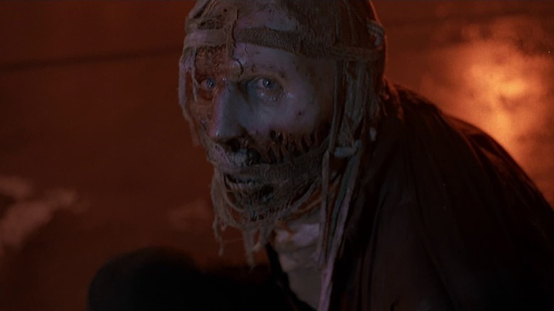 A disfigured Darkman (Liam Neeson) sitting in a flaming room in "Darkman."
