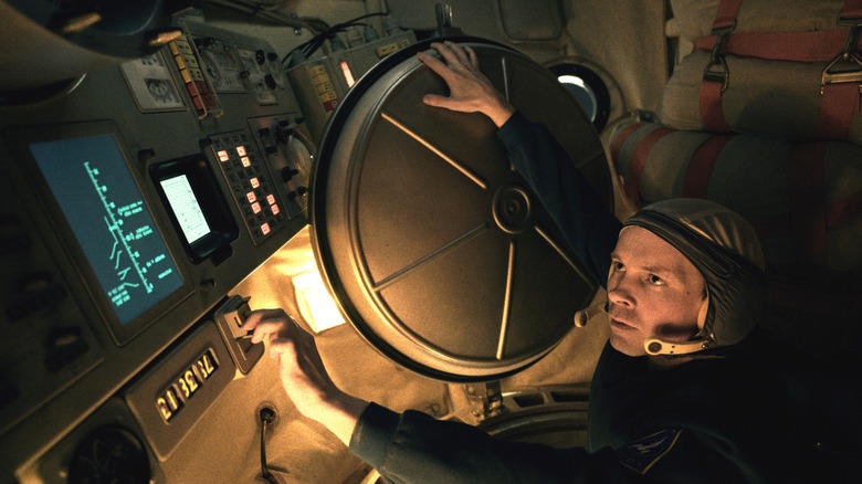 Sam Strike as Pavel Fetisov wearing an astronaut uniform and opening a hatch inside a space module in Star City