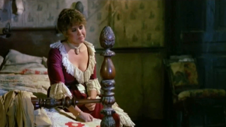 A woman in a victorian gown cries on a bed