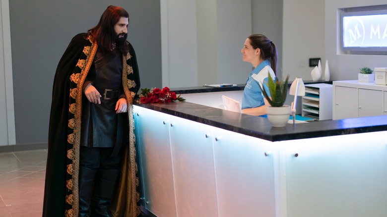 Nandor leans against a reception counter