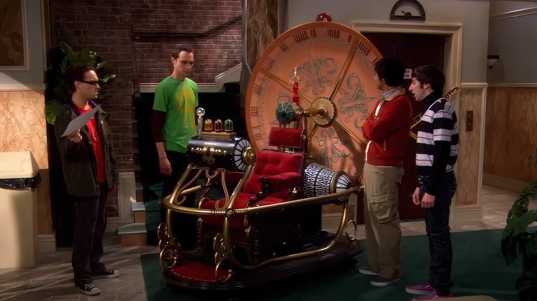 Raj, Leonard, Sheldon e Howard em pé em torno de uma máquina do tempo de réplica em 