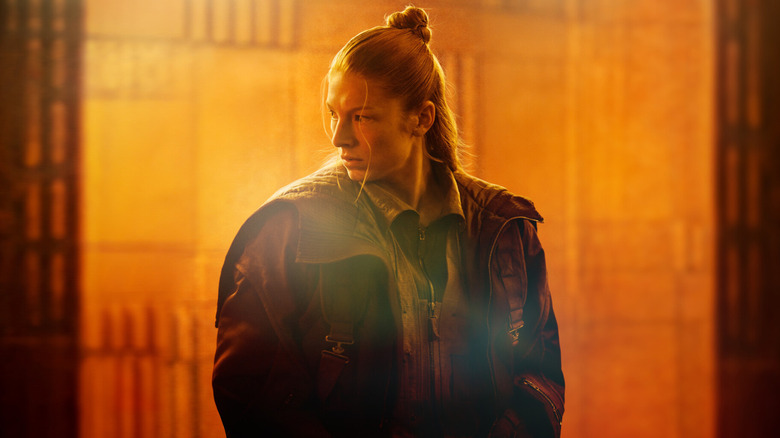 Hunter Schafer as Cora standing in front of a window lit in orange in Blade Runner 2099