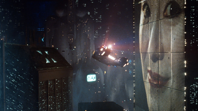 Bidikan lebar cakrawala Los Angeles di Blade Runner, termasuk mobil yang terbang di udara dan wanita di papan reklame raksasa