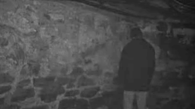 man standing facing the corner of a stone wall