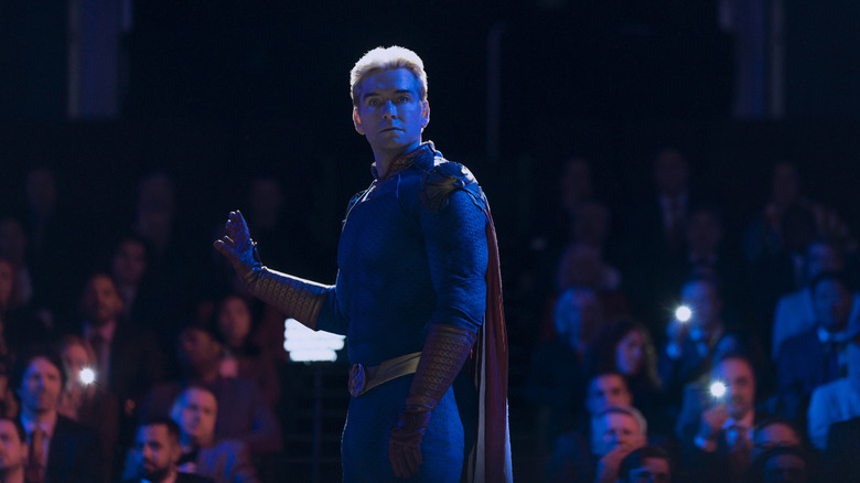 Antony Starr as Homelander standing in front of a crowd and lit by a blue screen in The Boys