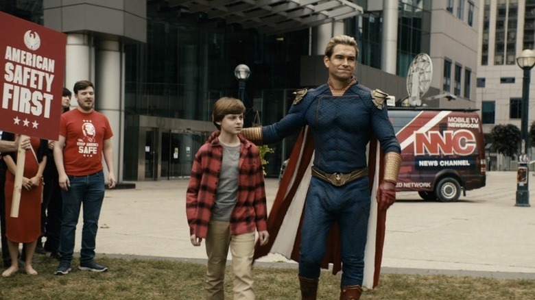 The Boys - Homelander walking with Ryan in front of protestor crowd