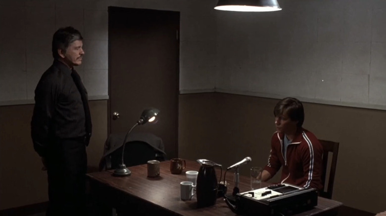 சார்லஸ் ப்ரோன்சனின் டிடெக்டிவ் லியோ கெஸ்லர் ஒரு விசாரணை அறையில் நிற்கிறார், ஜீன் டேவிஸின் வாரன் ஸ்டேசி 10 முதல் நள்ளிரவு வரை நாற்காலியில் அமர்ந்தார்