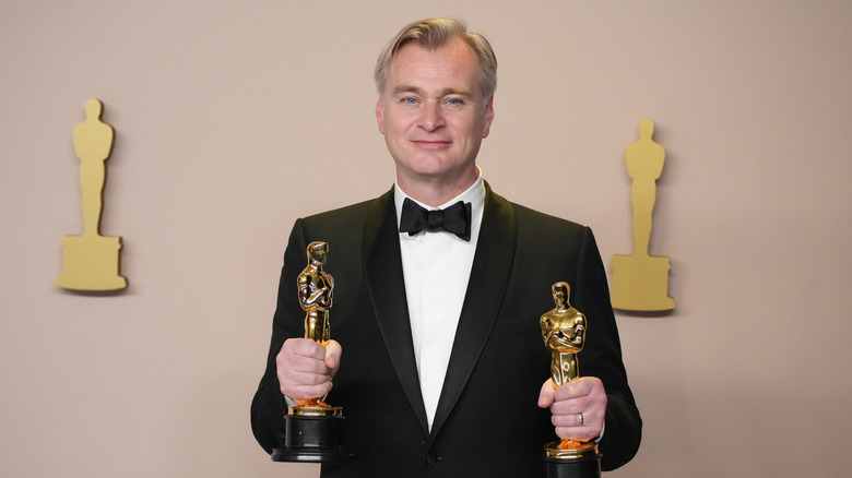 Christopher Nolan holds his two Oscar trophies while wearing a tuxedo at the Academy Awards
