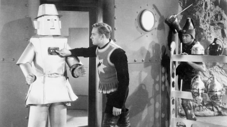 Gene Autry futzes with a robot as an assailant prepares to attack him in The Phantom Empire