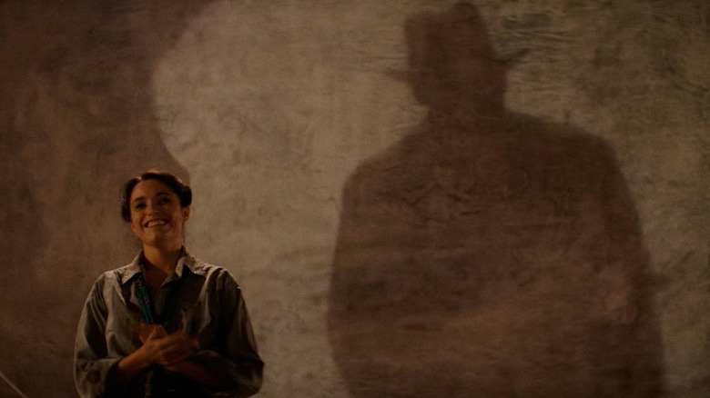 Karen Allen as Marion smiling as Indiana Jones' shadow is cast on the wall behind her in Raders of the Lost Ark