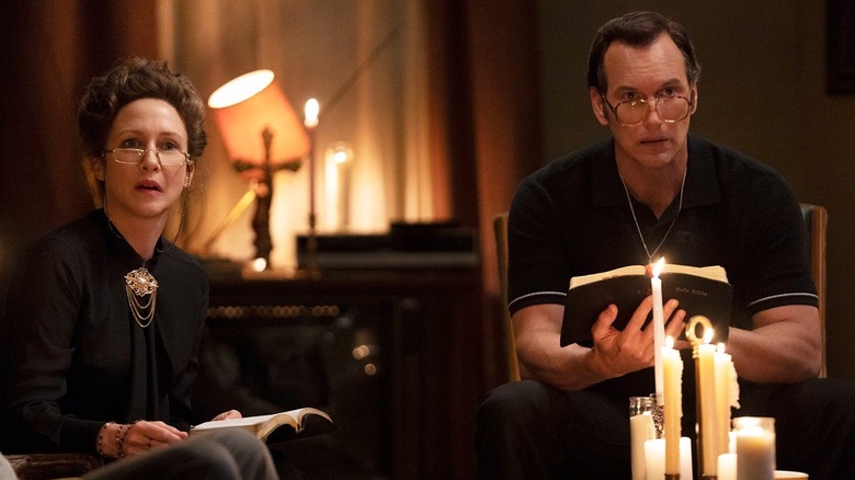 Vera Farmiga as Lorraine Warren and Patrick Wilson like Ed Warren holding Bibles and seated in front of candles in Conjuring 3