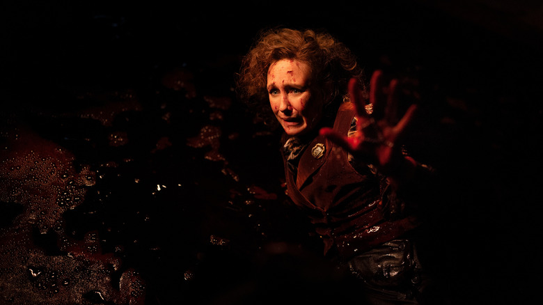 Vera Farmiga as Lorraine Warren defensively holding up her hand while laying in a pool of blood in The Conjuring: Last Rites