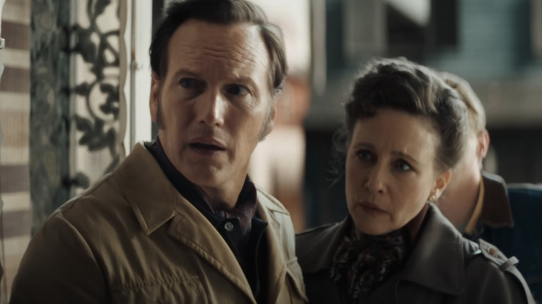 Patrick Wilson as Ed Warren and Vera Farmiga as Lorraine Warren standing outside a doorway with concerned looks on their faces in The Conjuring: Last Rites