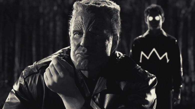 a man looking at a small object in his hand with another man in shadow with white eyes behind him