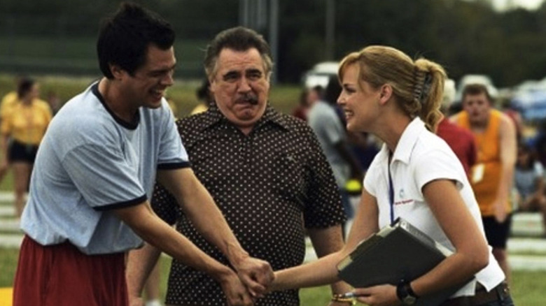 a man in gym shorts and a shirt laughing next to a woman with a clipboard