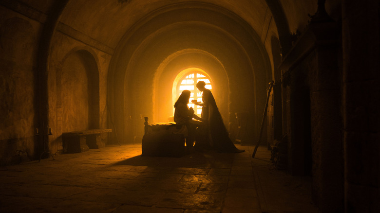 Robin Hood and Sister Brigid are bathed in orange light in a dark room in The Death of Robin Hood