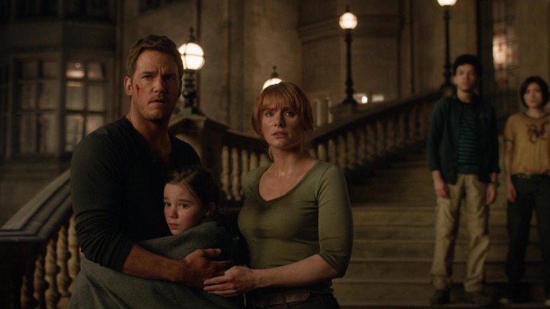 Owen and Claire hug Charlotte as they look in shock from outside a manor in Jurassic World: Dominion