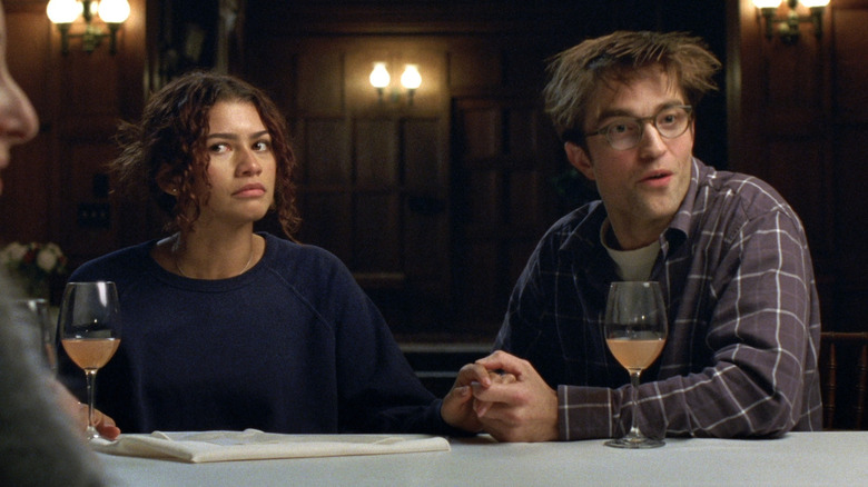 Zendaya as Emma seated at a dinner table with a concerned look on her face next to Robert Pattinson as Charlie in The Drama