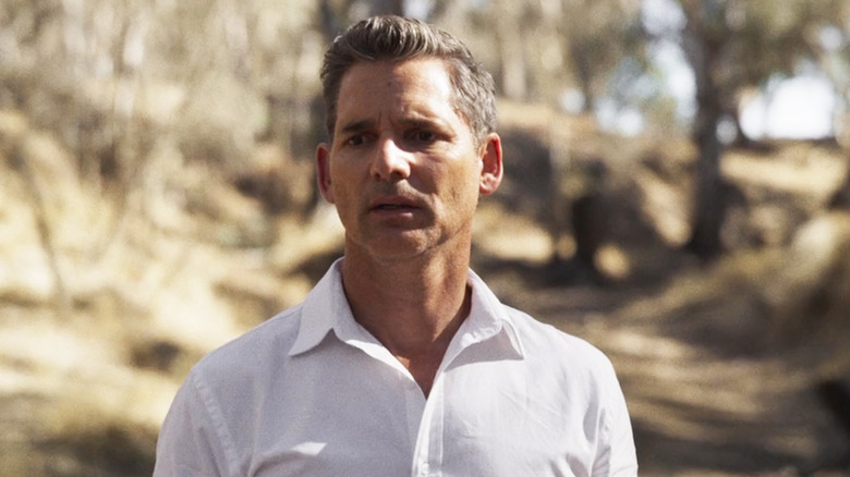 Eric Bana's Aaron Falk stands in a wooded area looking worried in The Dry