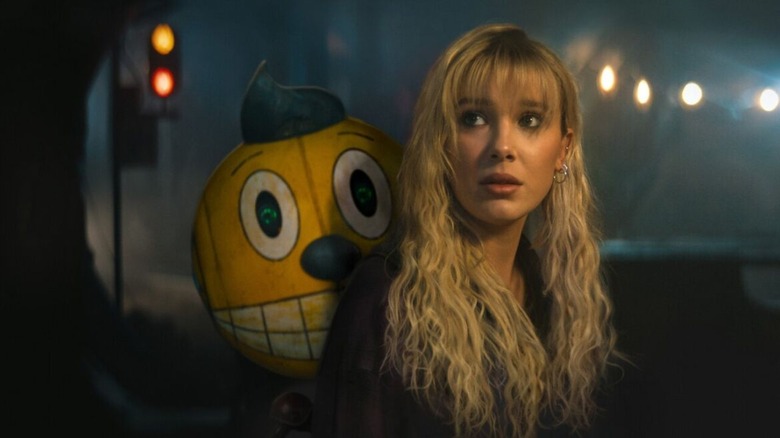 Michelle and a smiling, yellow-faced robot, out on the streets at night. A scene from The Electric State.