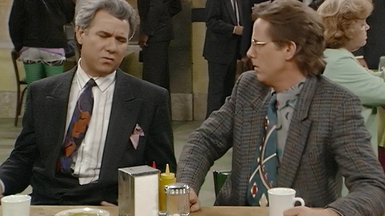 John Larroquette as Reinhold Daniel Fielding Elmore seated at a table on the night field