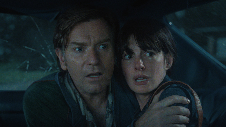 Ewan McGregor as Greg Platt and Anne Hathaway Denise Platt holding onto each other and looking scared inside a car with a cracked window in The End of Oak Street