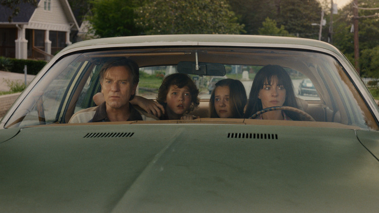Ewan McGregor as Greg Platt and Anne Hathaway as Denise Platt sitting in a car with Christian Convery as Brian Platt and Maisy Stella as Audrey Platt in The End of Oak Street