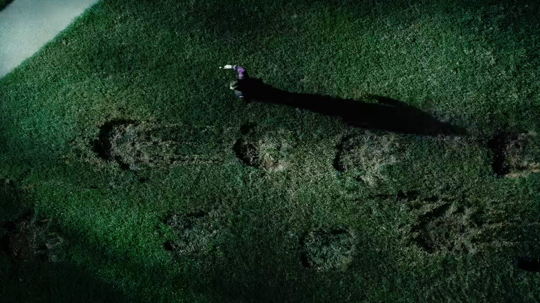 A set of giant dinosaur footprints on a lawn at night in The End of Oak Street