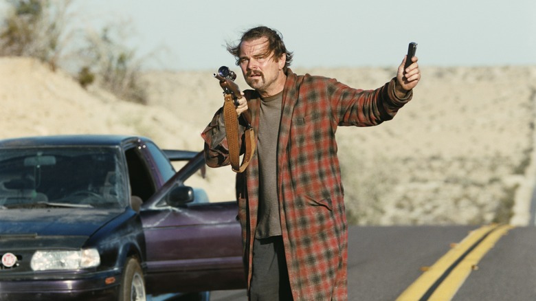 Bob walking down a desert road with a scoped rifle in a bathrobe in One Battle After Another
