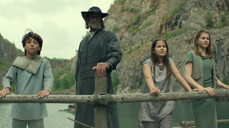Children stand with a man wearing a hat on a bridge in Foundation season 3