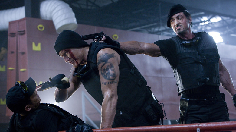 Barney Ross pointing a gun at Gunner Jensen as he attacks Yin Yang in The Expendables