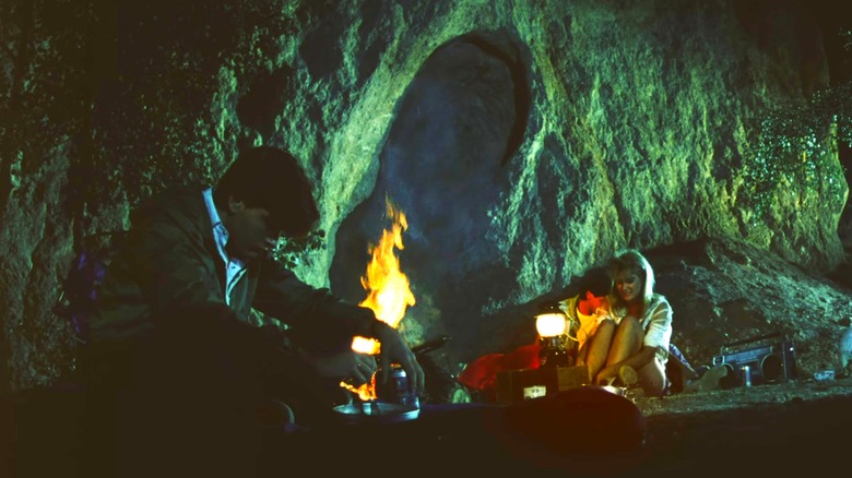 Charlie Sheen as Lance sitting with his head down in front of a campfire where Laura Dern as Tina and George Clooney as Ron are canoodling in Grizzly II: Revenge