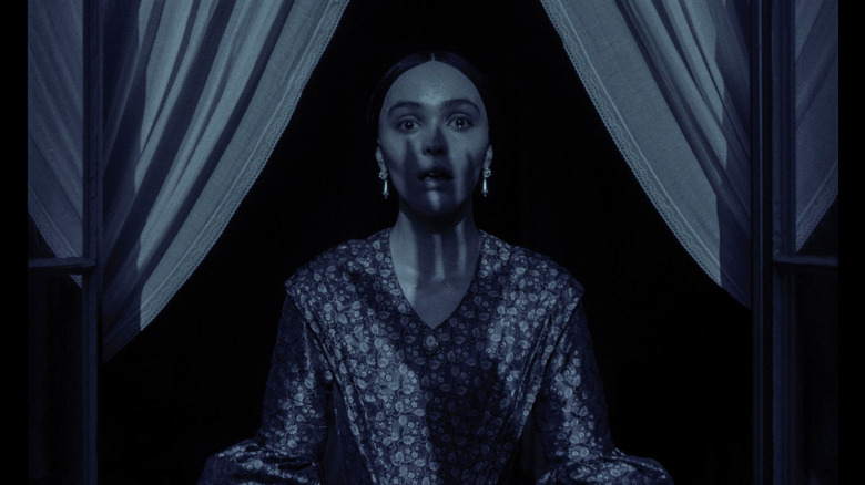 Ellen parada em choque em uma janela olhando para a sombra de uma mão em Nosferatu