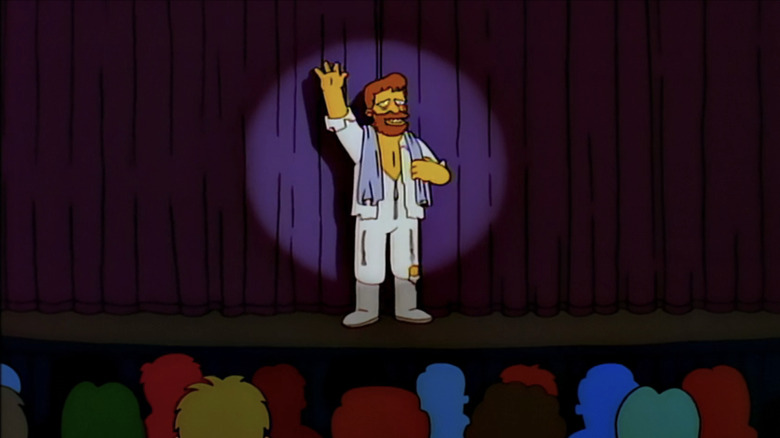 Troy McClure stands on-stage in front of a curtain in The Simpsons